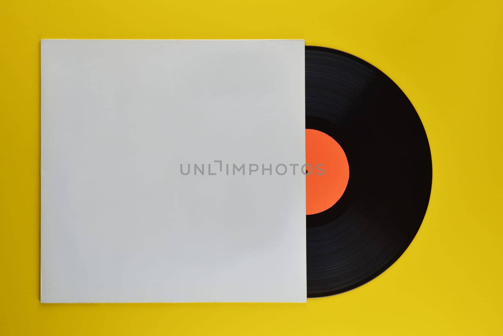 old black vinyl record with blank orange label halfway out of its white blank cover on yellow background