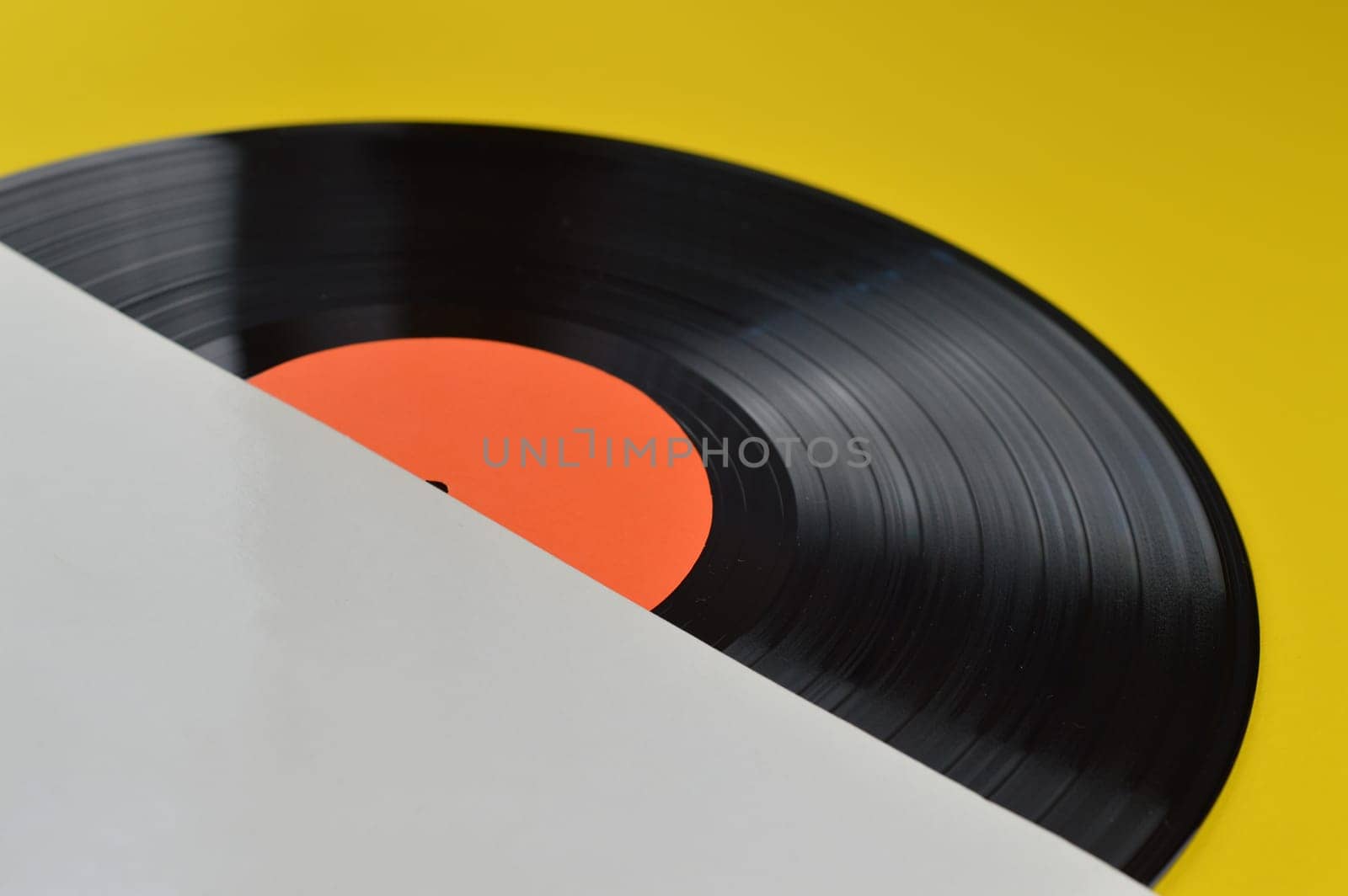 old black vinyl record with blank orange label halfway out of its white blank cover on yellow background