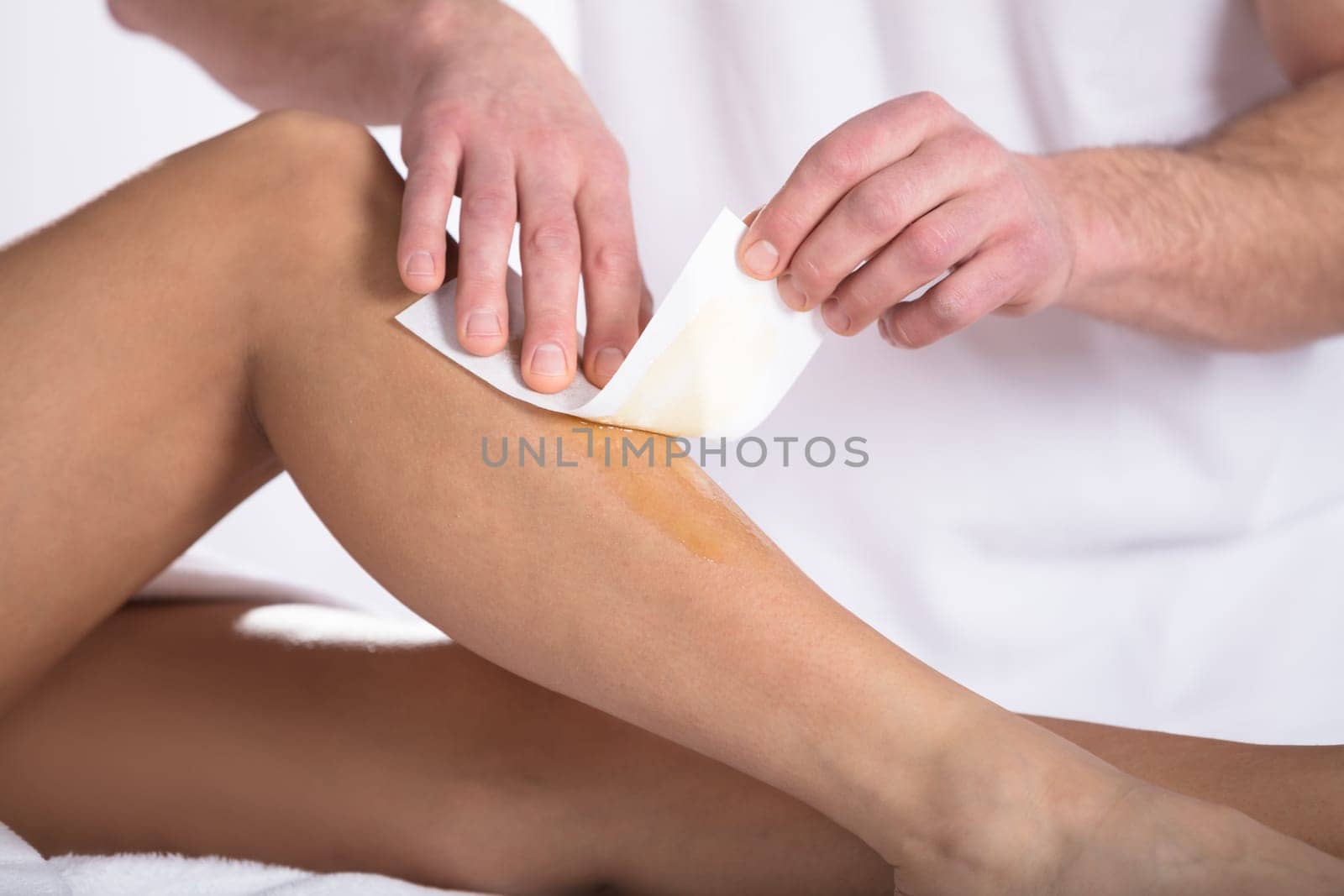 Therapist Waxing Woman's Leg With Wax Strip In Beauty Spa