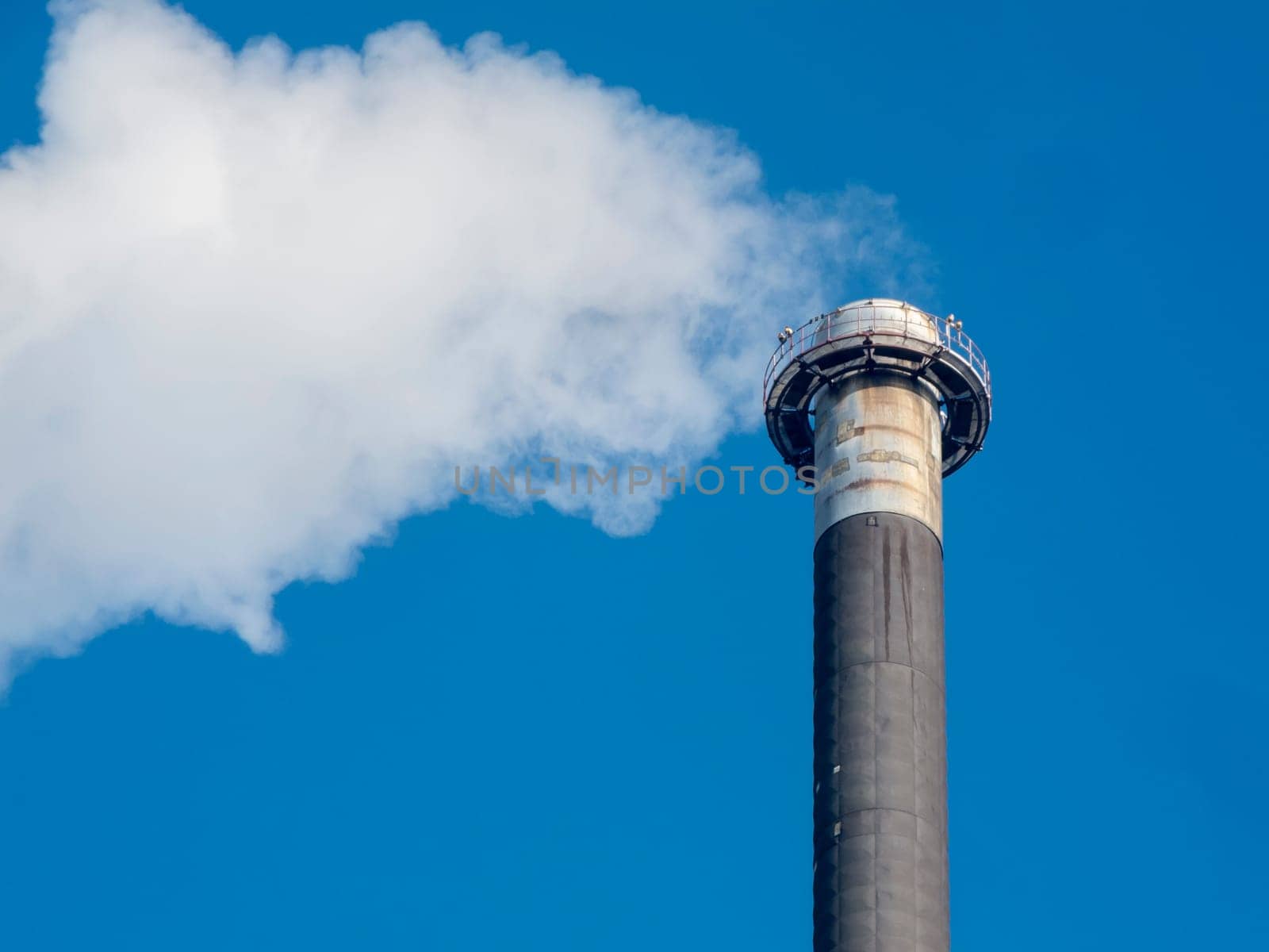 View of an industrial chimney of a power plant with white smoke in front of a blue sky