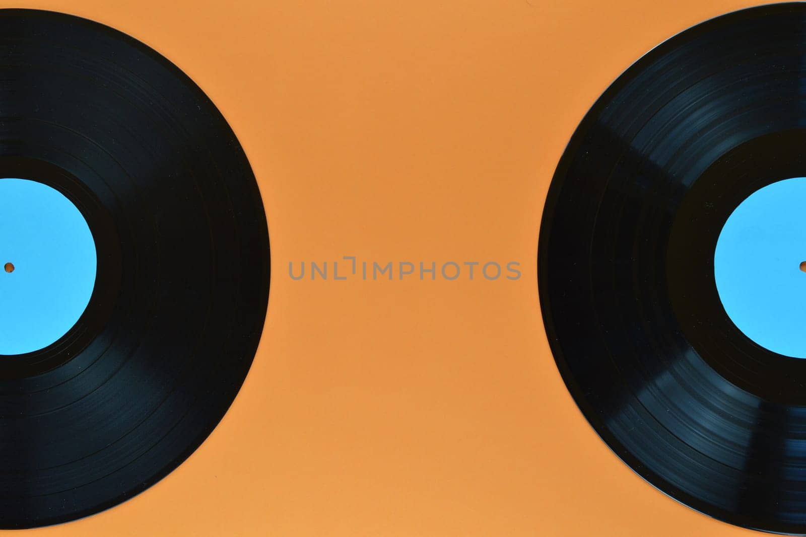 two old black vinyl records with blank cyan labels on orange background