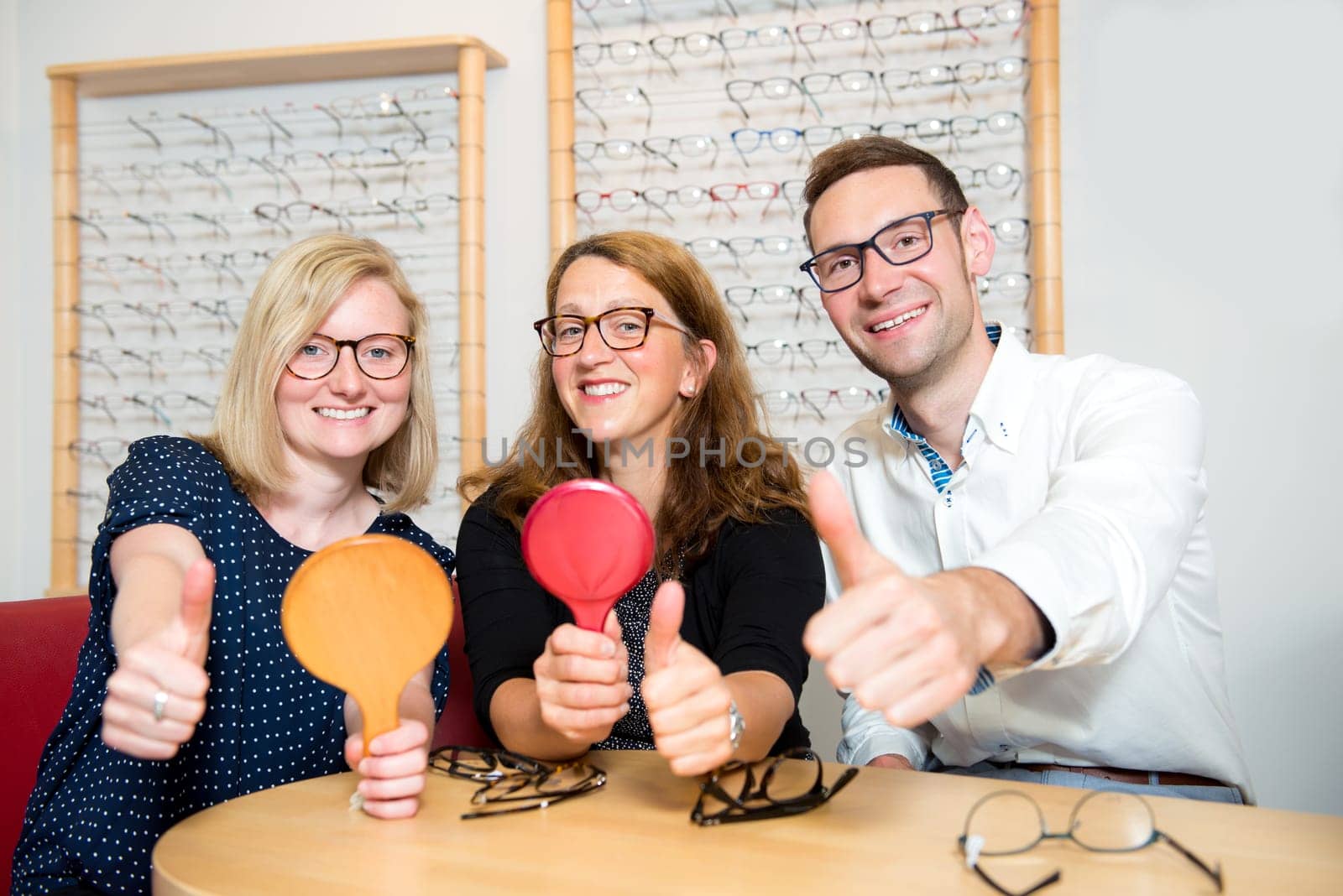 in optician shop-two women and one man with thumb up selecting new glasses