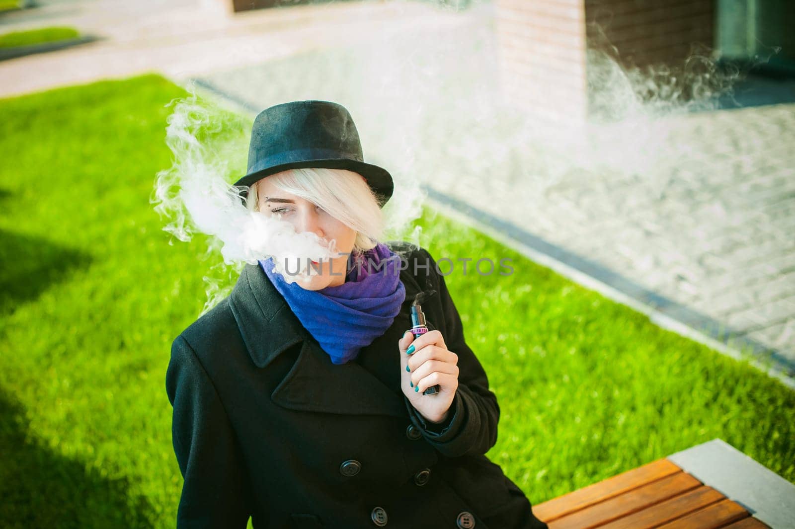 portrait of young beautiful woman with white hair, in a black coat, a skirt and a black hat, smoking an electronic cigarette, blowing the smoke vapor
