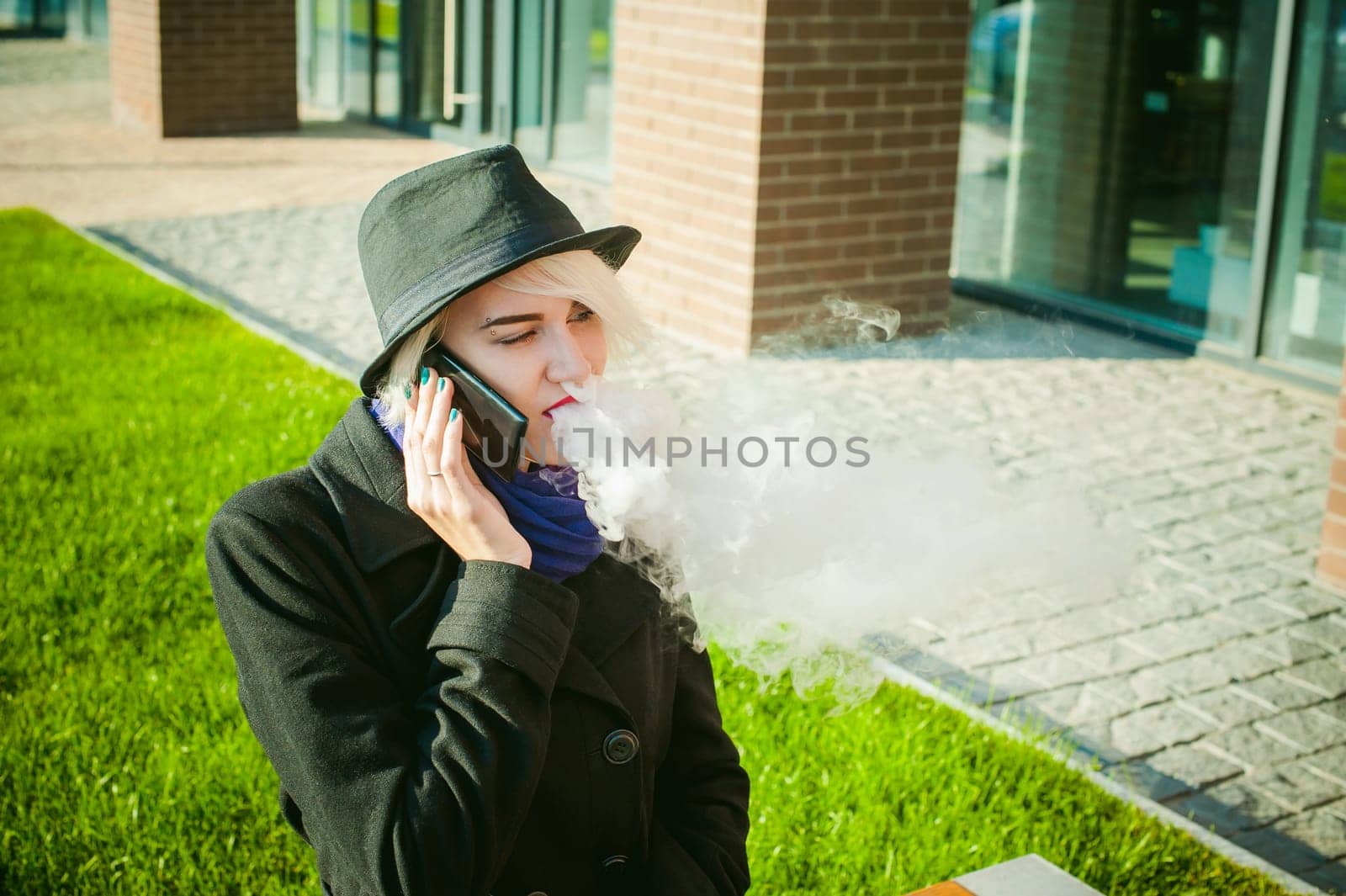 portrait of young beautiful woman with white hair, in a black coat, a skirt and a black hat, talking on cell phone on the street. telephone communication, liaison, pleasant conversation about the business