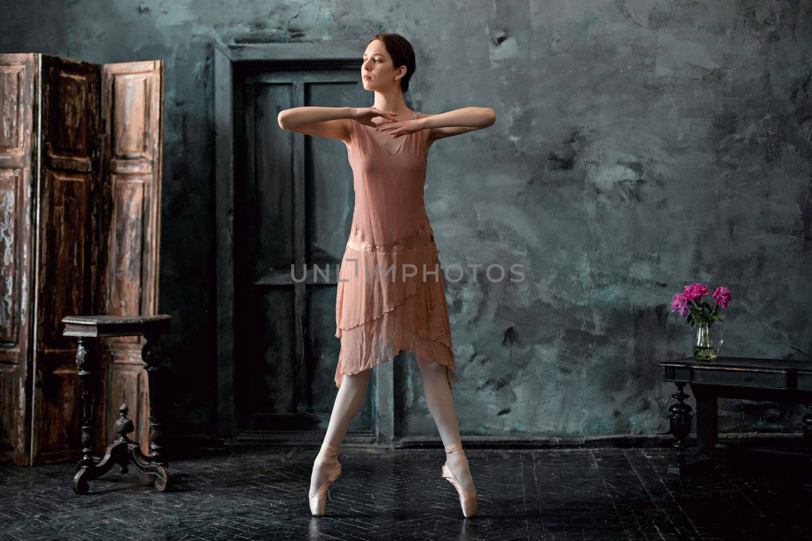 Young and incredibly beautiful ballerina is posing and dancing in a black wooden studio