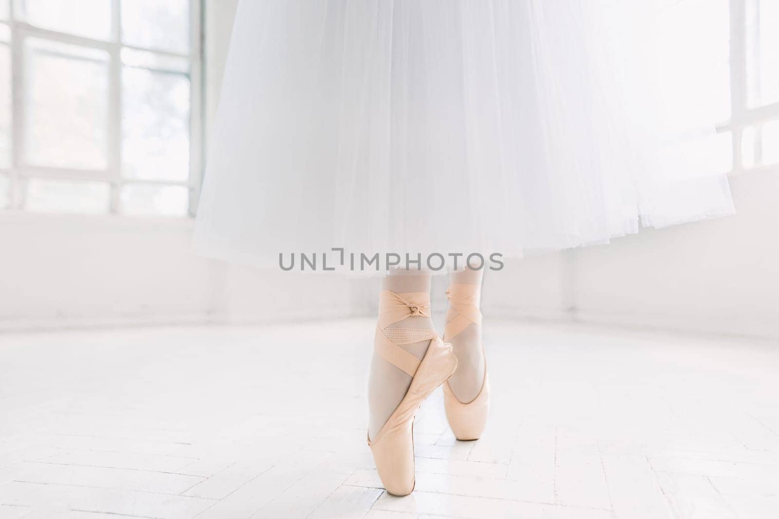 Young ballerina dancing, closeup on legs and shoes, standing in pointe position.