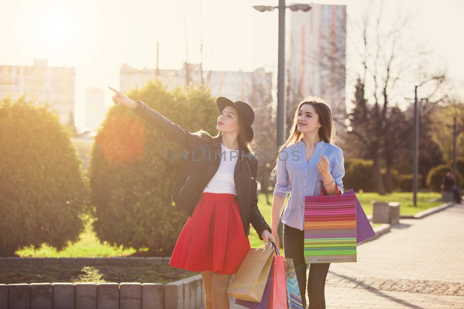 Two girls walking with shopping bags on city streets at sunny day