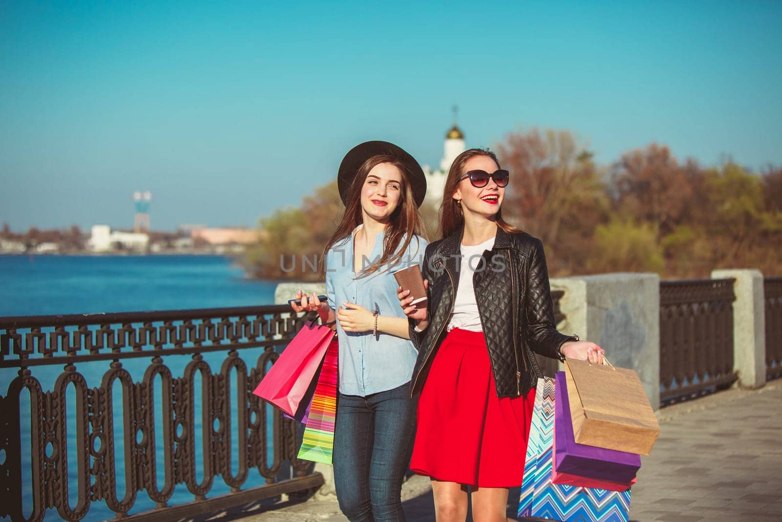 Two girls walking with shopping bags on city streets at sunny day