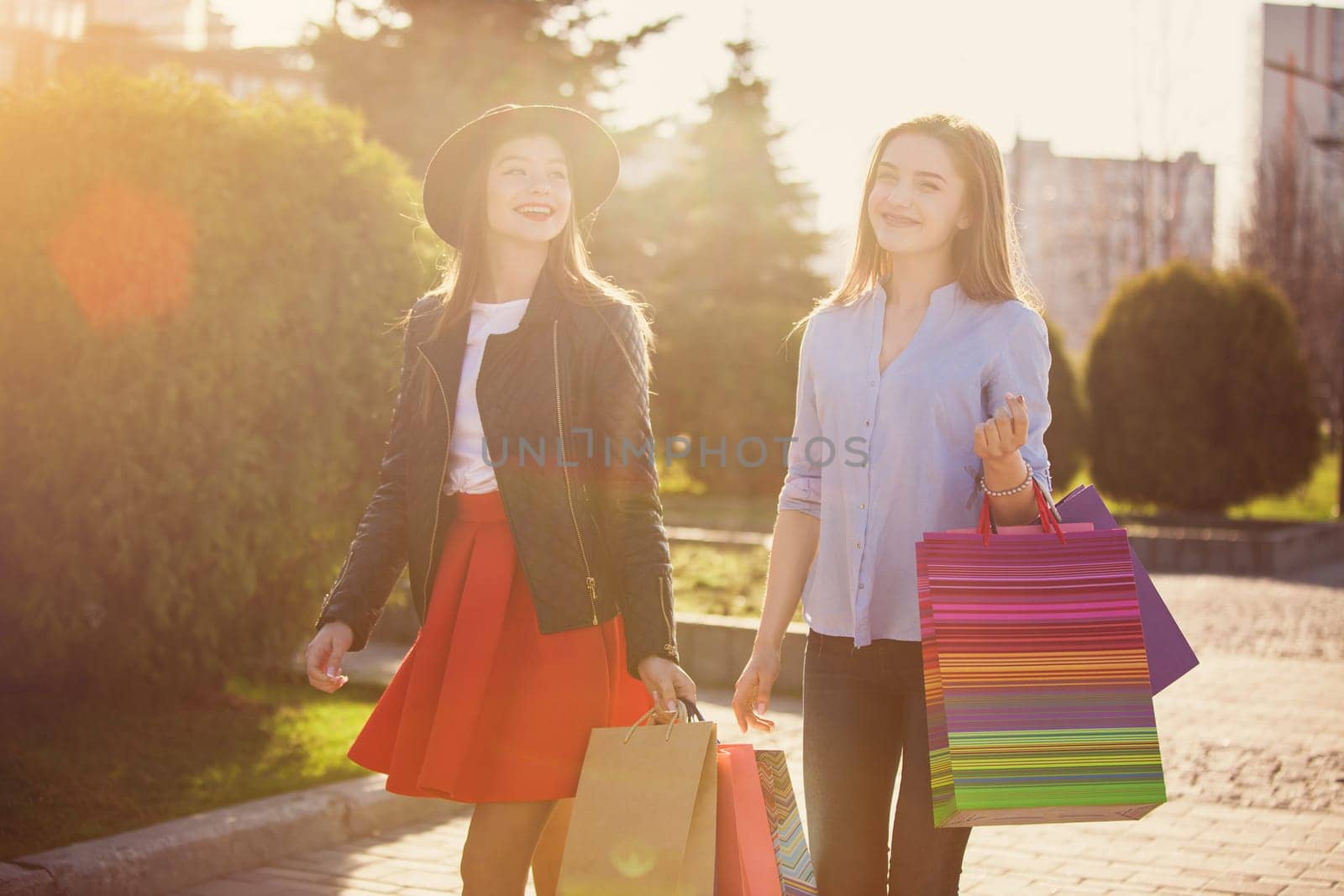 Two girls walking with shopping bags on city streets at sunny day