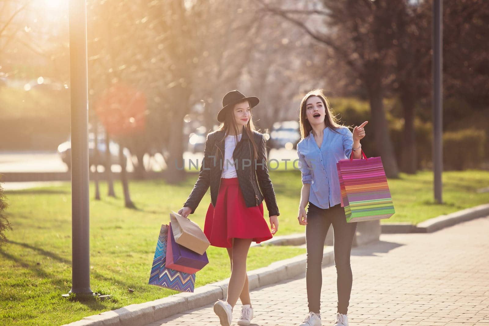 Two girls walking with shopping bags on city streets at sunny day