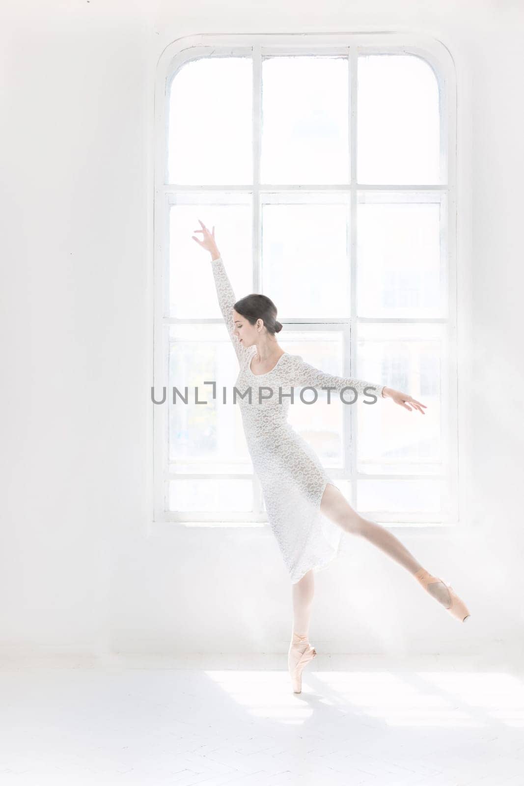 Young and incredibly beautiful ballerina is posing and dancing in a white studio full of light.