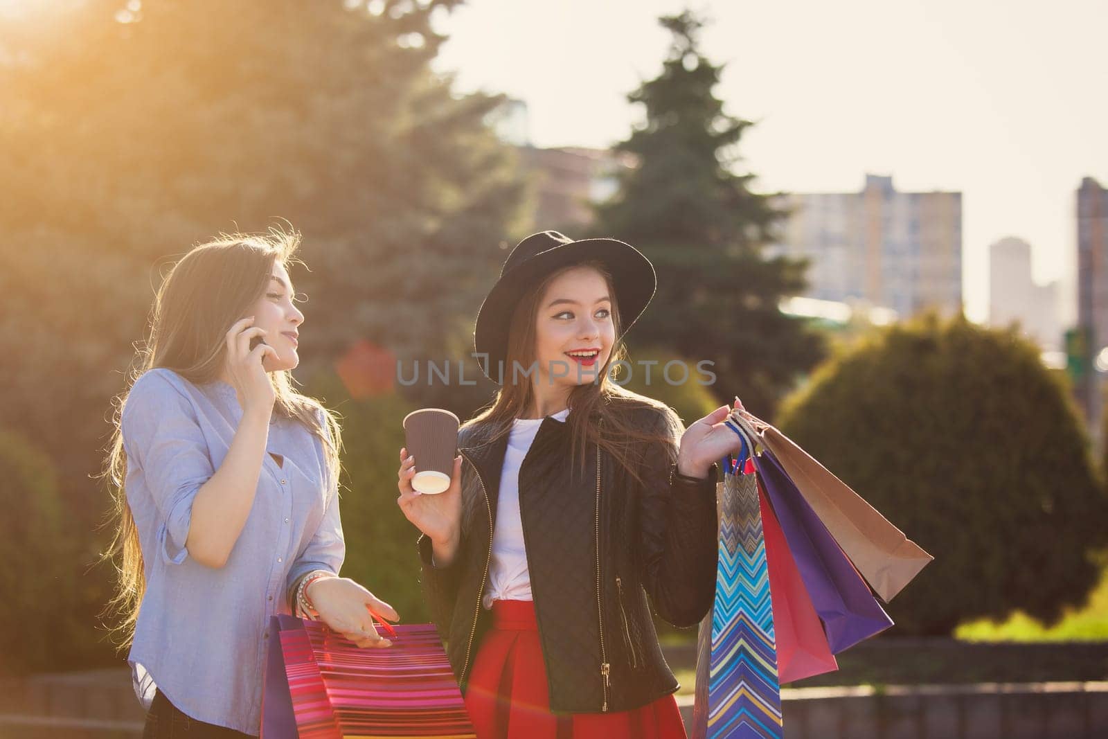 Two girls walking with shopping bags on city streets at sunny day