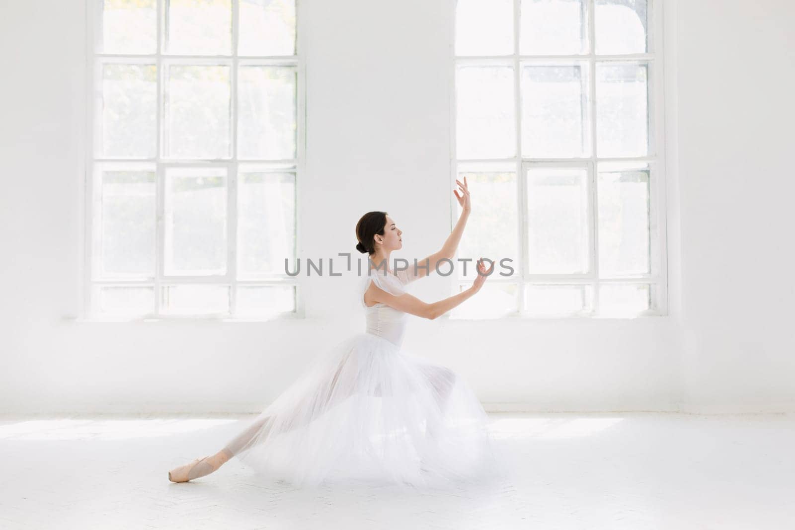 Young and incredibly beautiful ballerina is posing and dancing in a white studio full of light.