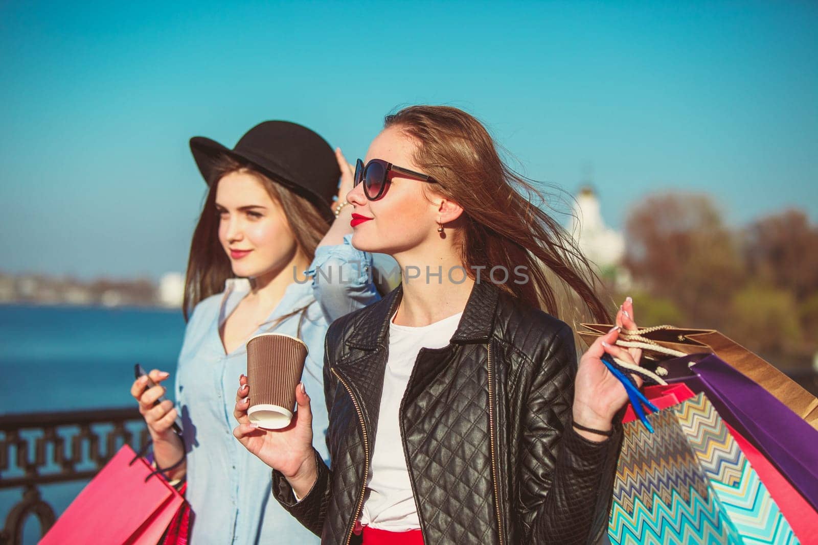 Two girls walking with shopping bags on city streets at sunny day