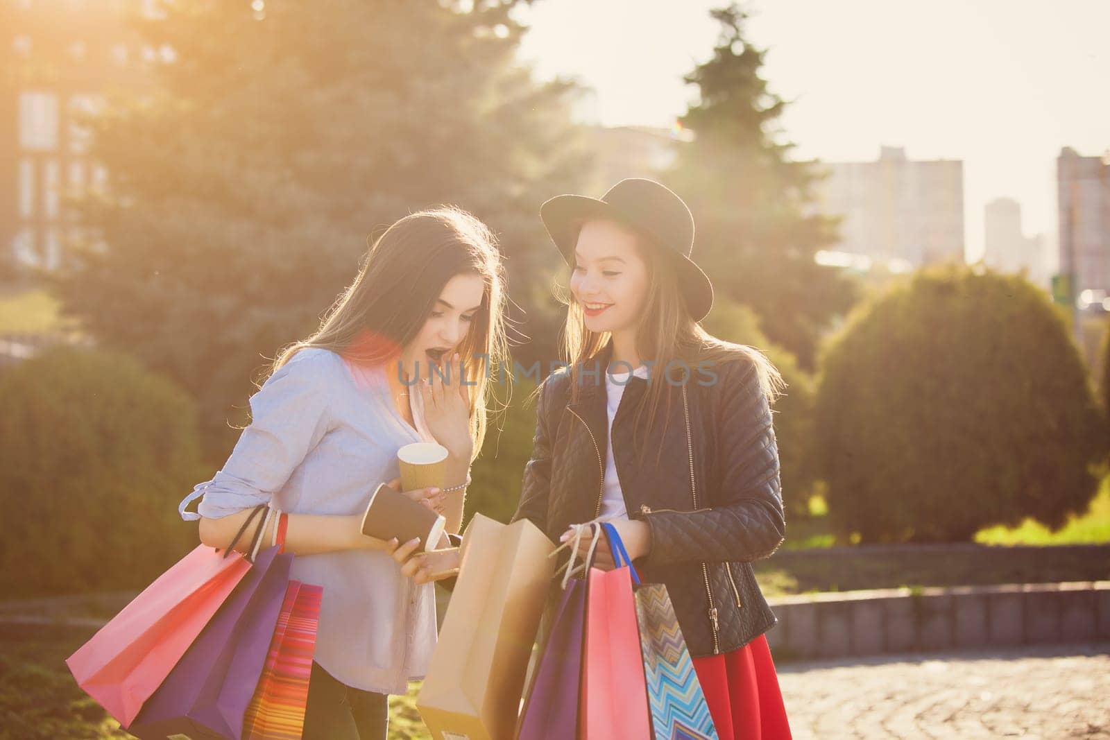 Two girls walking with shopping bags on city streets at sunny day