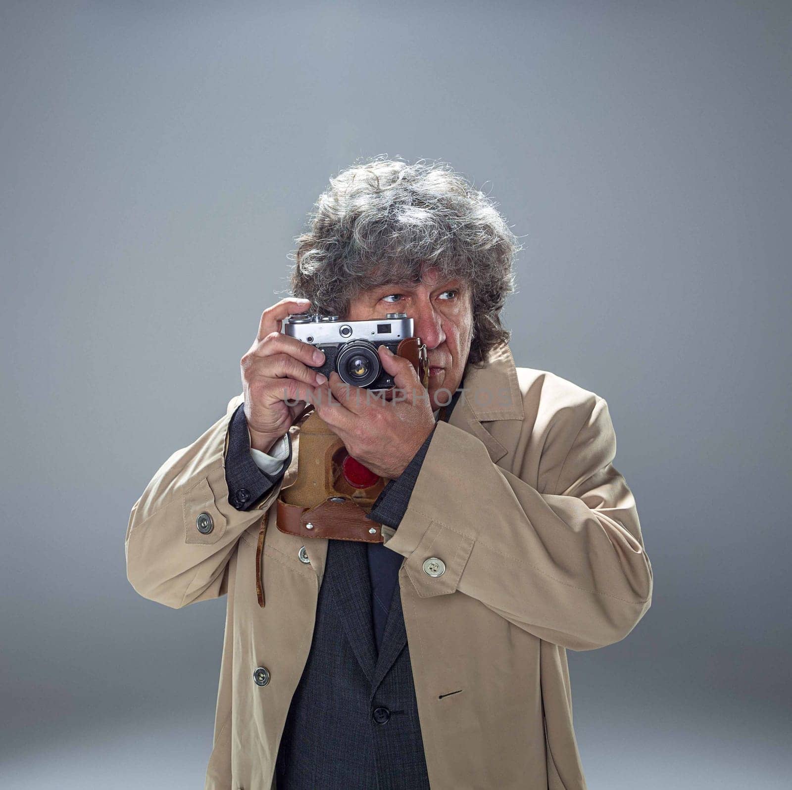 The senior man in cloak as detective or mafia boss with photo camera. Studio shot on gray in retro stile