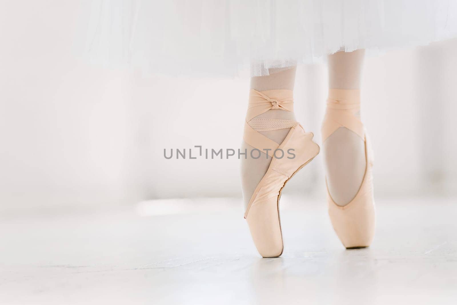 Young ballerina dancing, closeup on legs and shoes, standing in pointe position.
