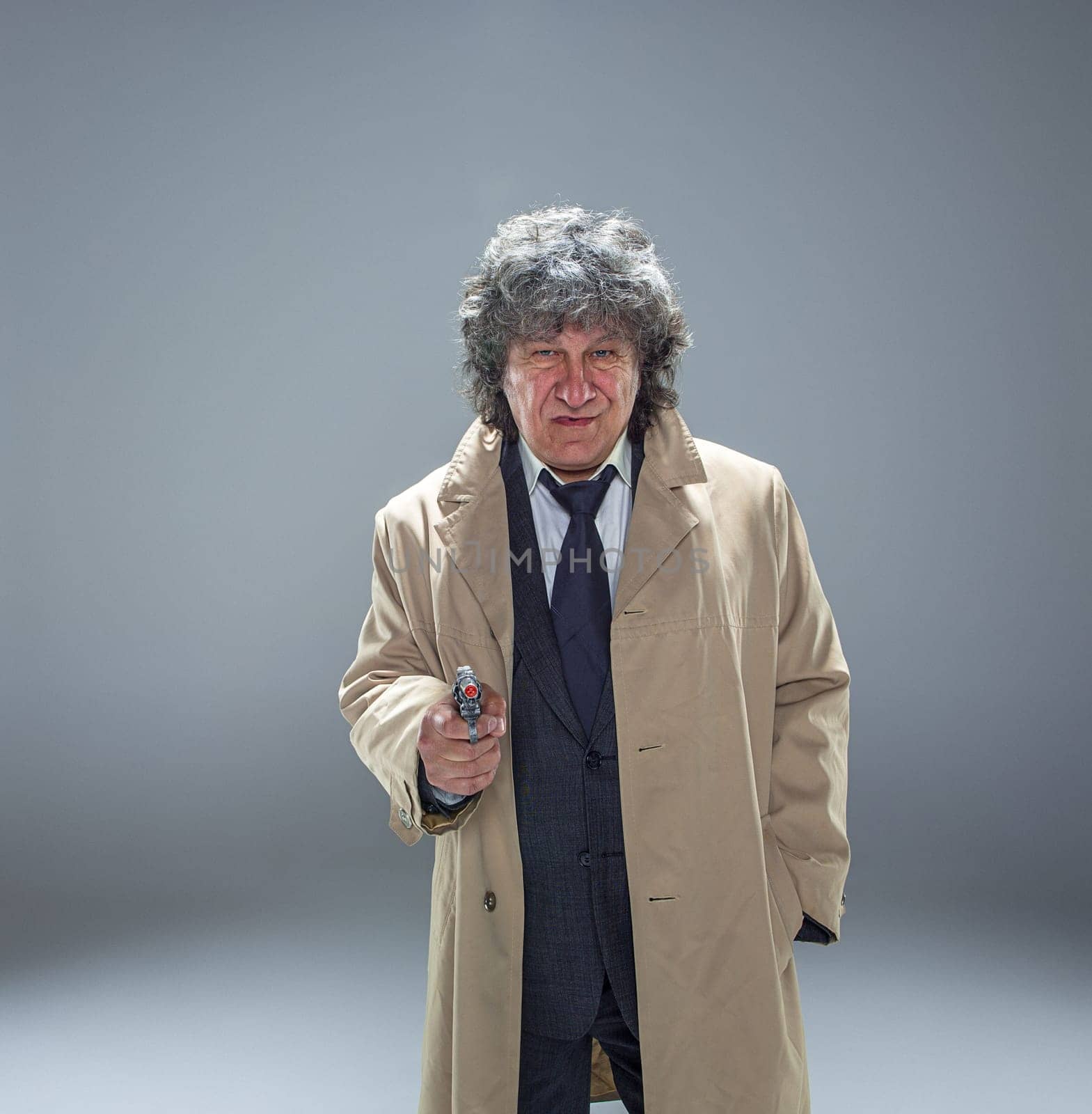 Senior police agent with a gun standing as detective or mafia boss. Studio shot on gray in retro stile