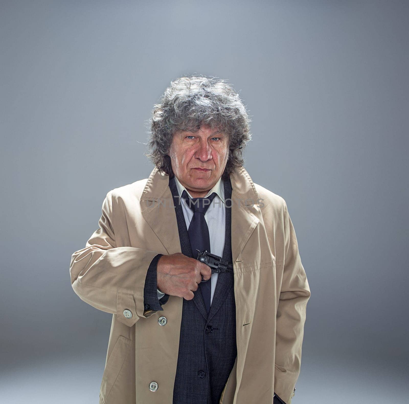Senior police agent with a gun standing as detective or mafia boss. Studio shot on gray in retro stile