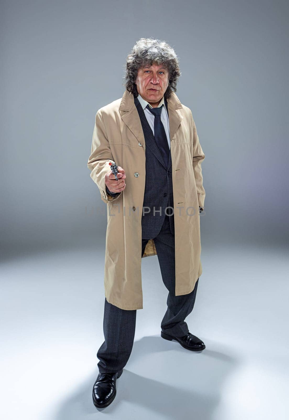 Senior police agent with a gun standing as detective or mafia boss. Studio shot on gray in retro stile