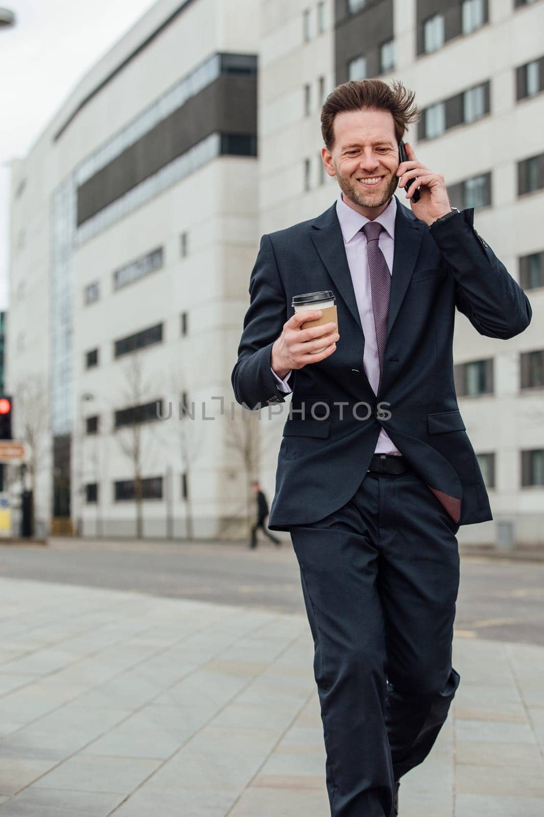 Businessman is walking to work in the city. He is holding a coffee cup and is talking on the phone.