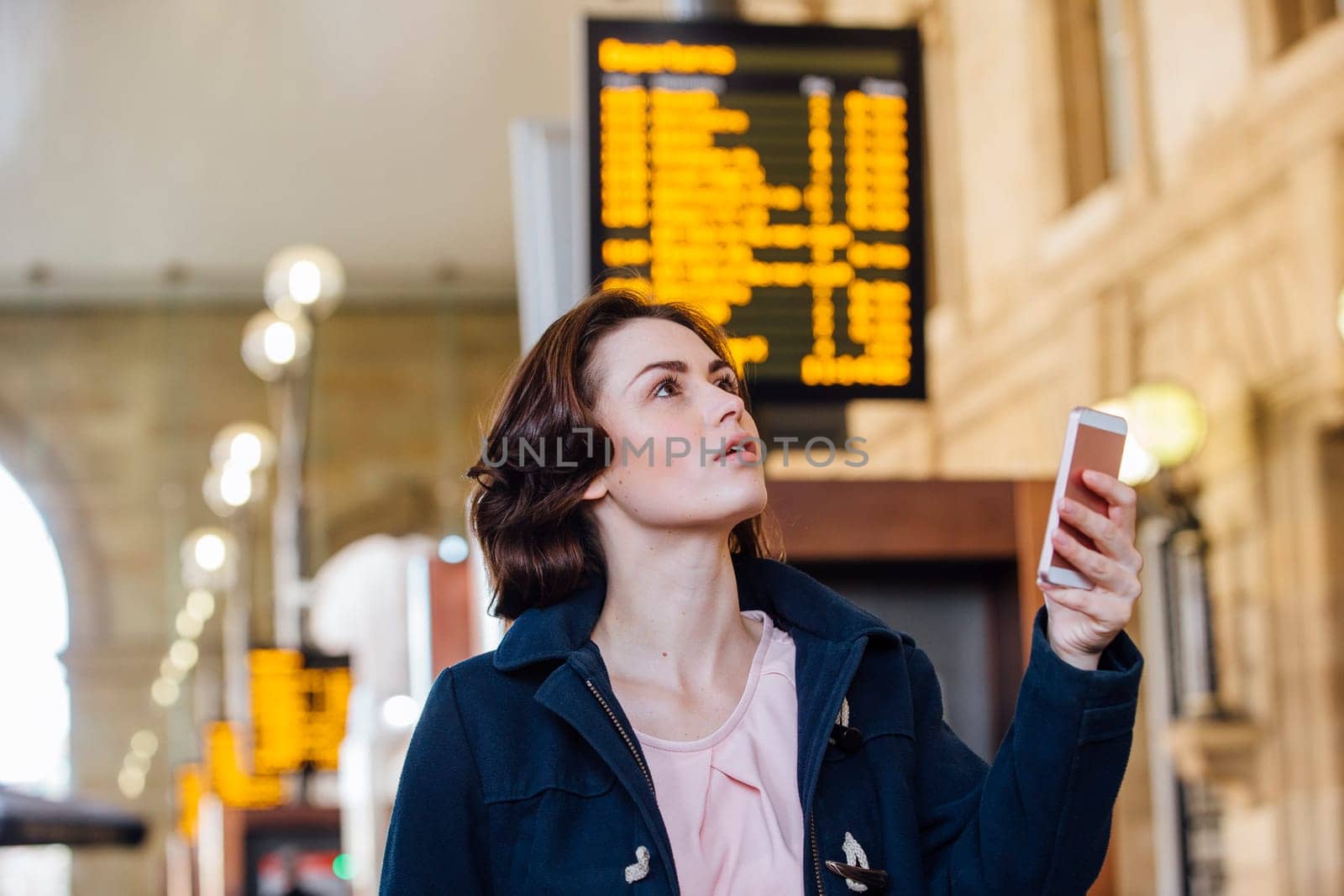 Young businesswoman is using her smart phone to check for her train time on the departure board.