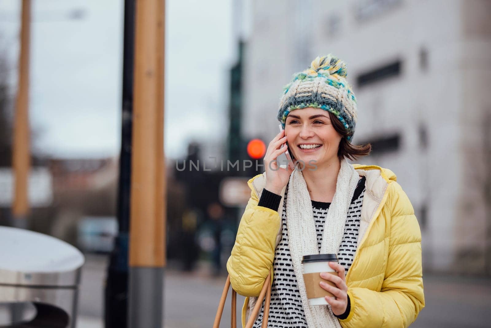 Woman is walking in the city with a coffee cup while talking on the phone.