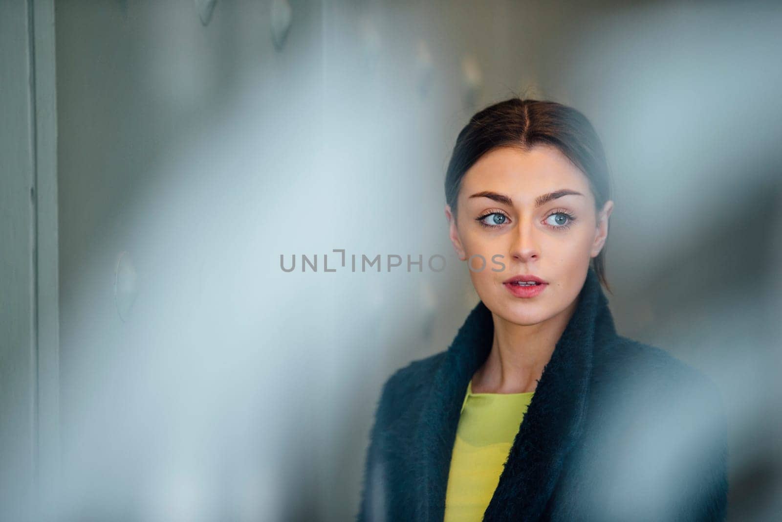 Businesswoman is standing in her workplace, looking out of her office window.