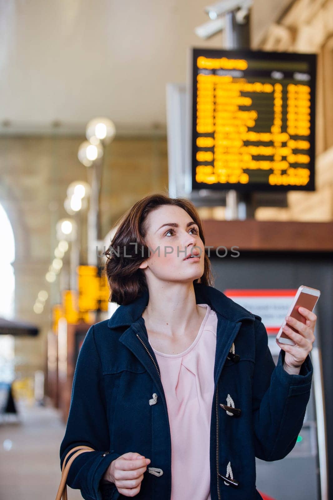 Young businesswoman is using her smart phone to check for her train time on the departure board.