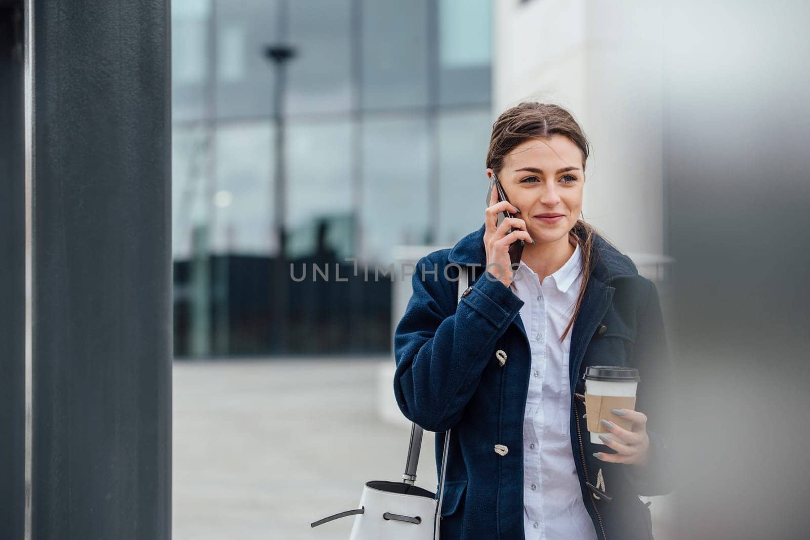 Businesswoman is walking to work in the city. She is holding a coffee cup and is talking on the phone.