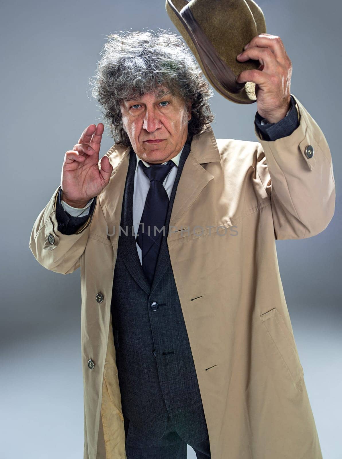 The senior man in cloak as detective or mafia boss. Studio shot on gray in retro stile. Mature man with hat and suitcase