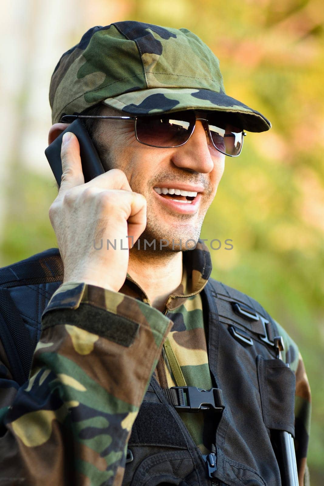 The smiling soldier in uniform is calling, talking, using phone.