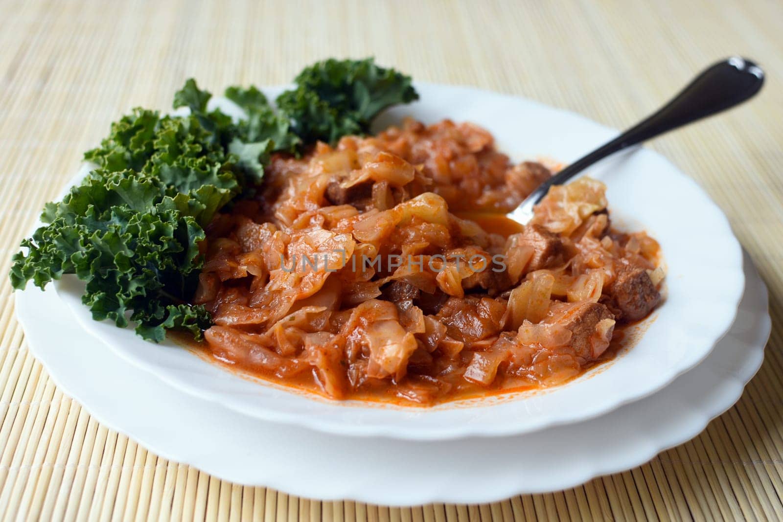 Cooked cabbage with meat is in white plate.