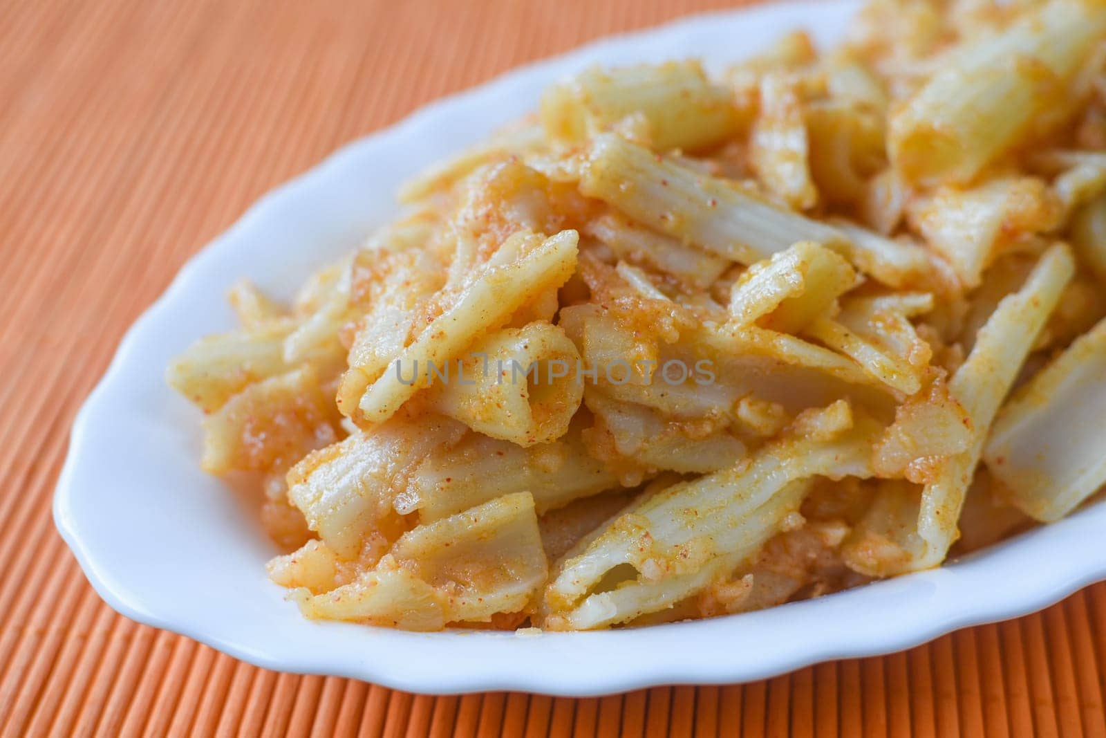 Pasta with potato is on white dish on orange background.