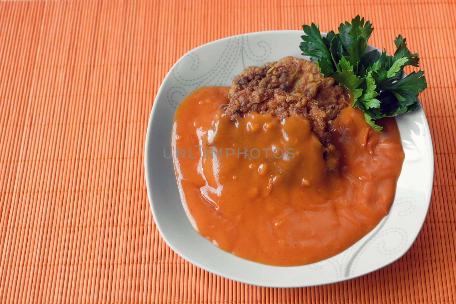 Meatballs in tomato sauce is in white plate on orange background.