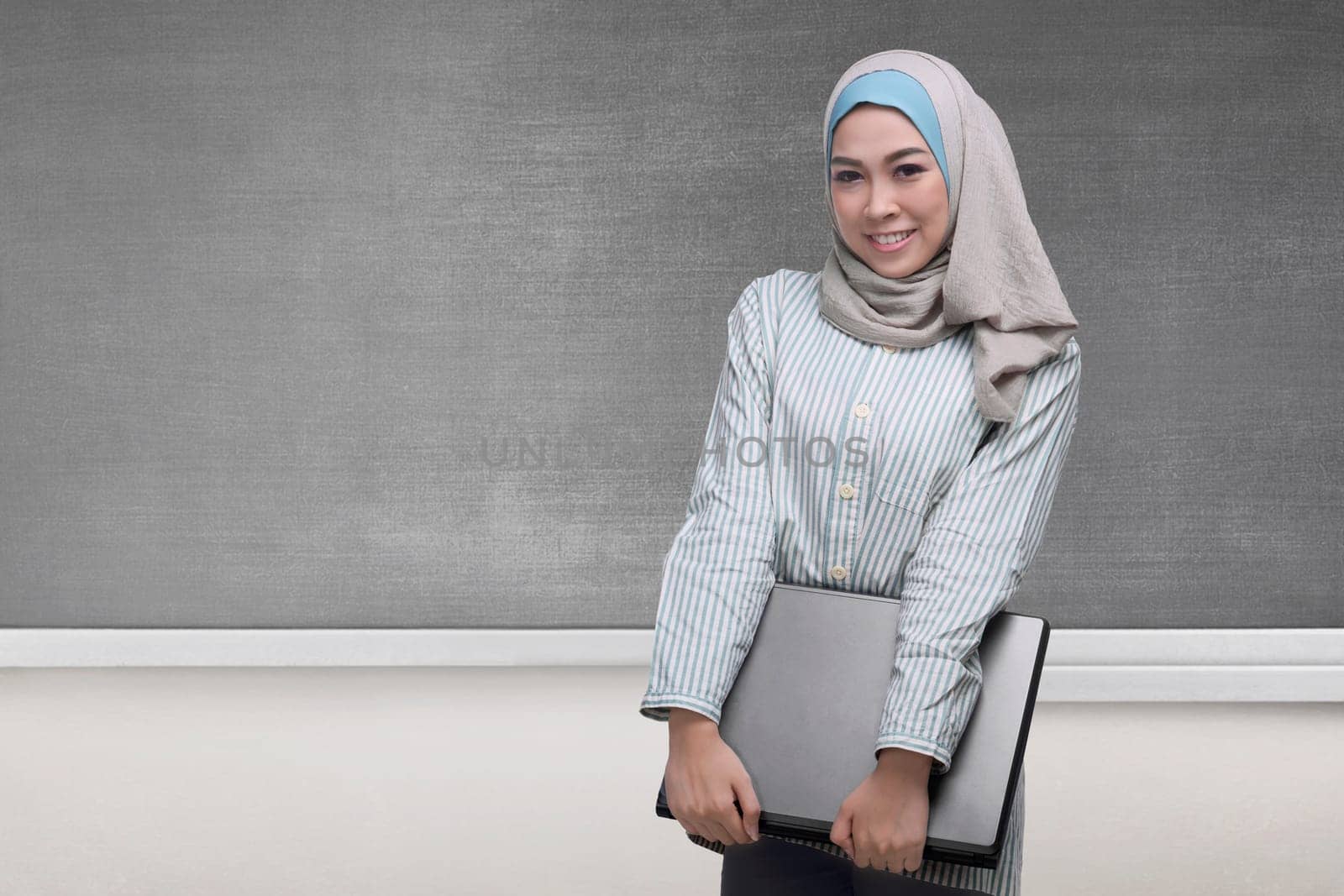 Pretty asian muslim woman holding a laptop with blackboard background