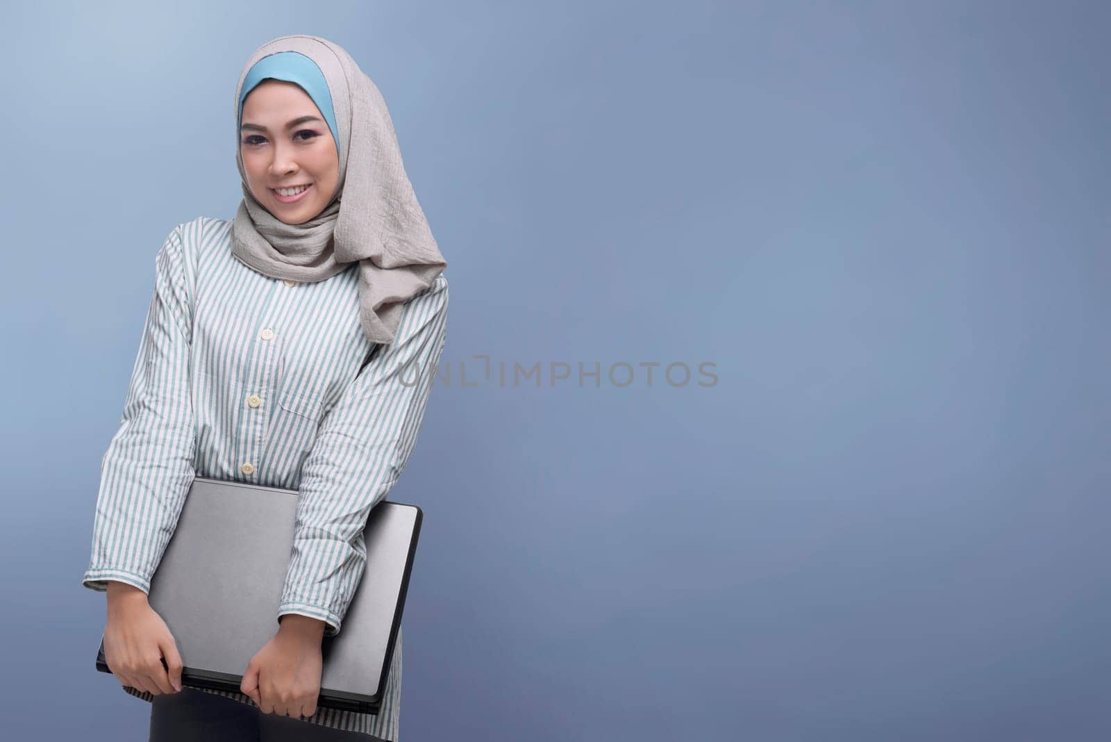 Young asian muslim woman holding laptop against bright background