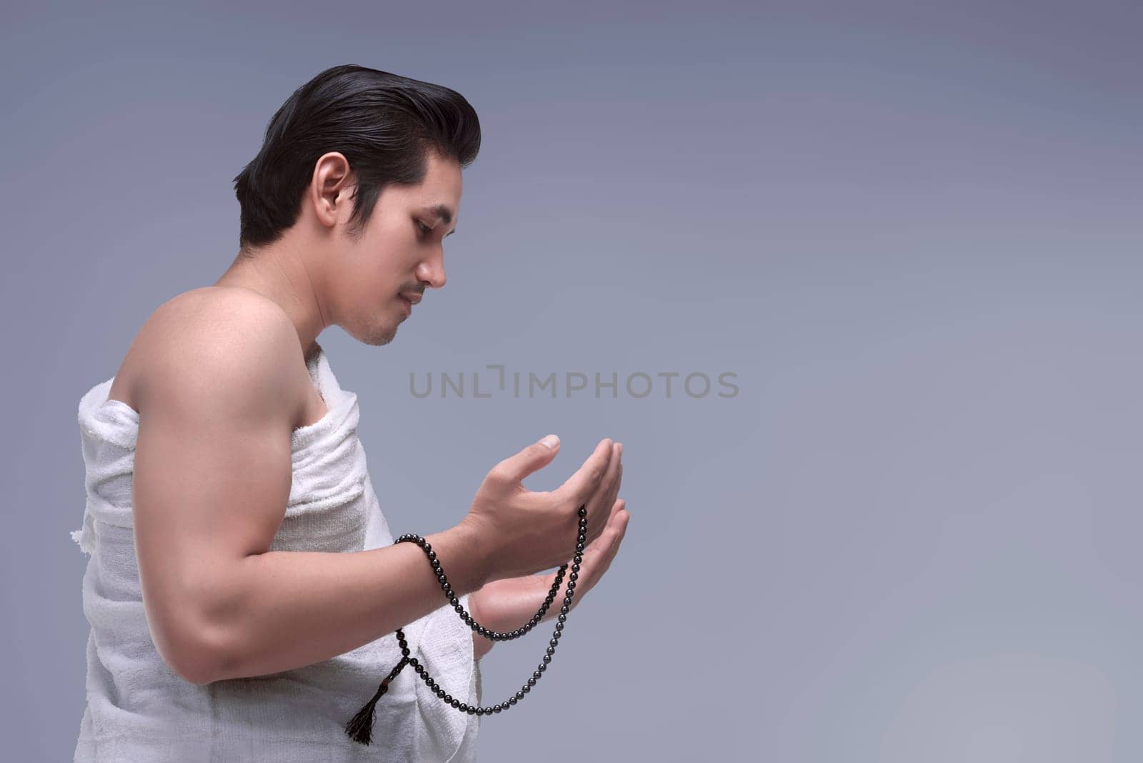 Religious asian muslim man in ihram praying with prayer beads over dark bacground
