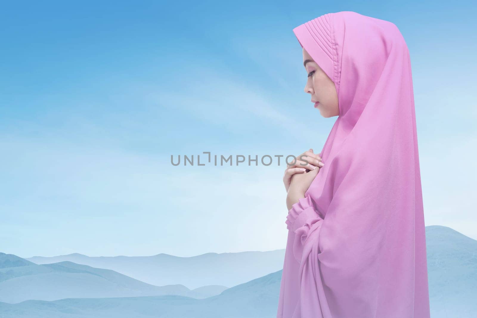 Beautiful asian muslim woman wearing hijab praying over bright sky