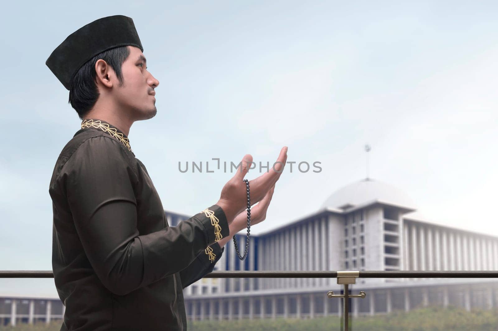 Religious asian muslim man in traidional dress praying to god with mosque backgroud