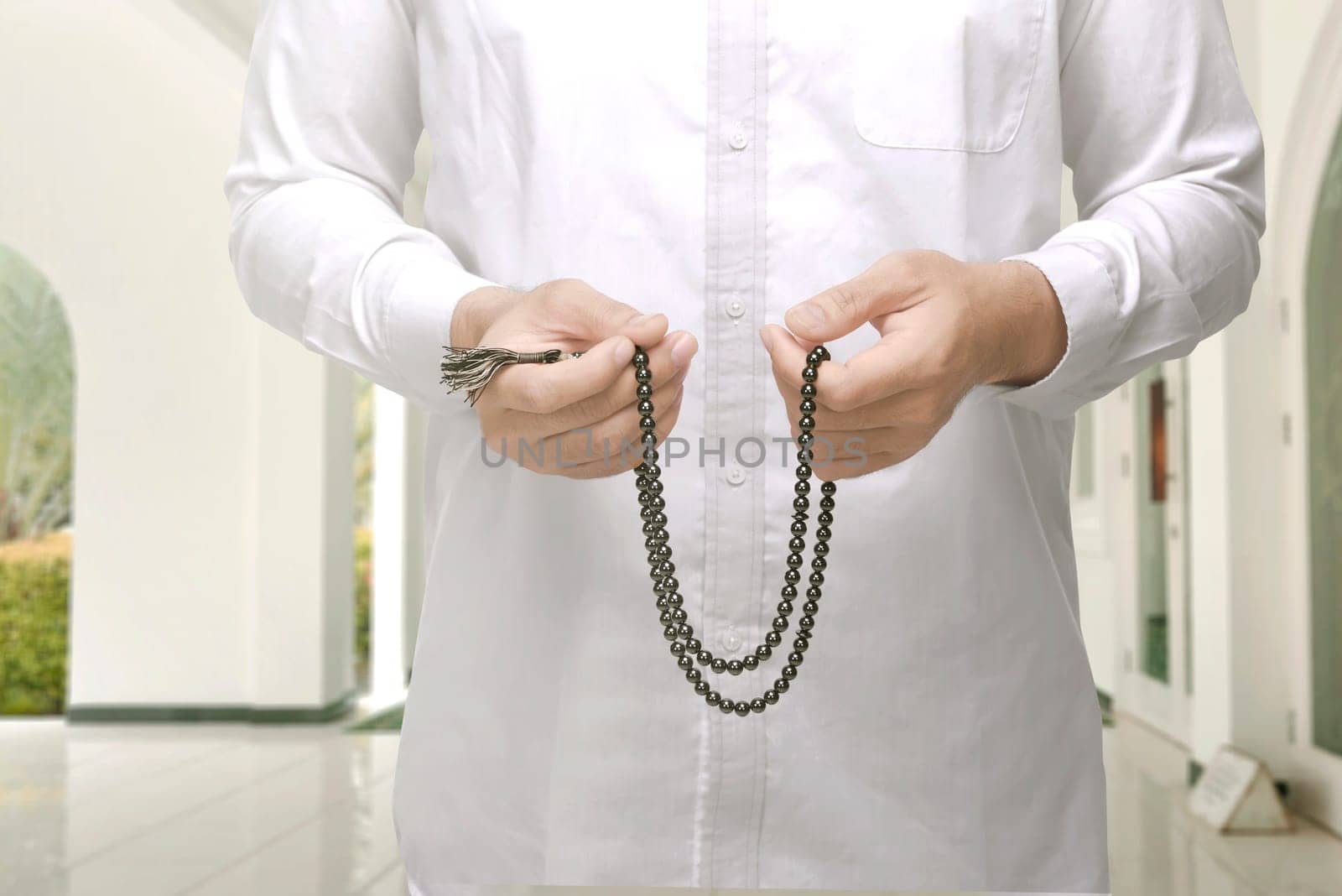Muslim man raising hand and praying with prayer beads inside the mosque