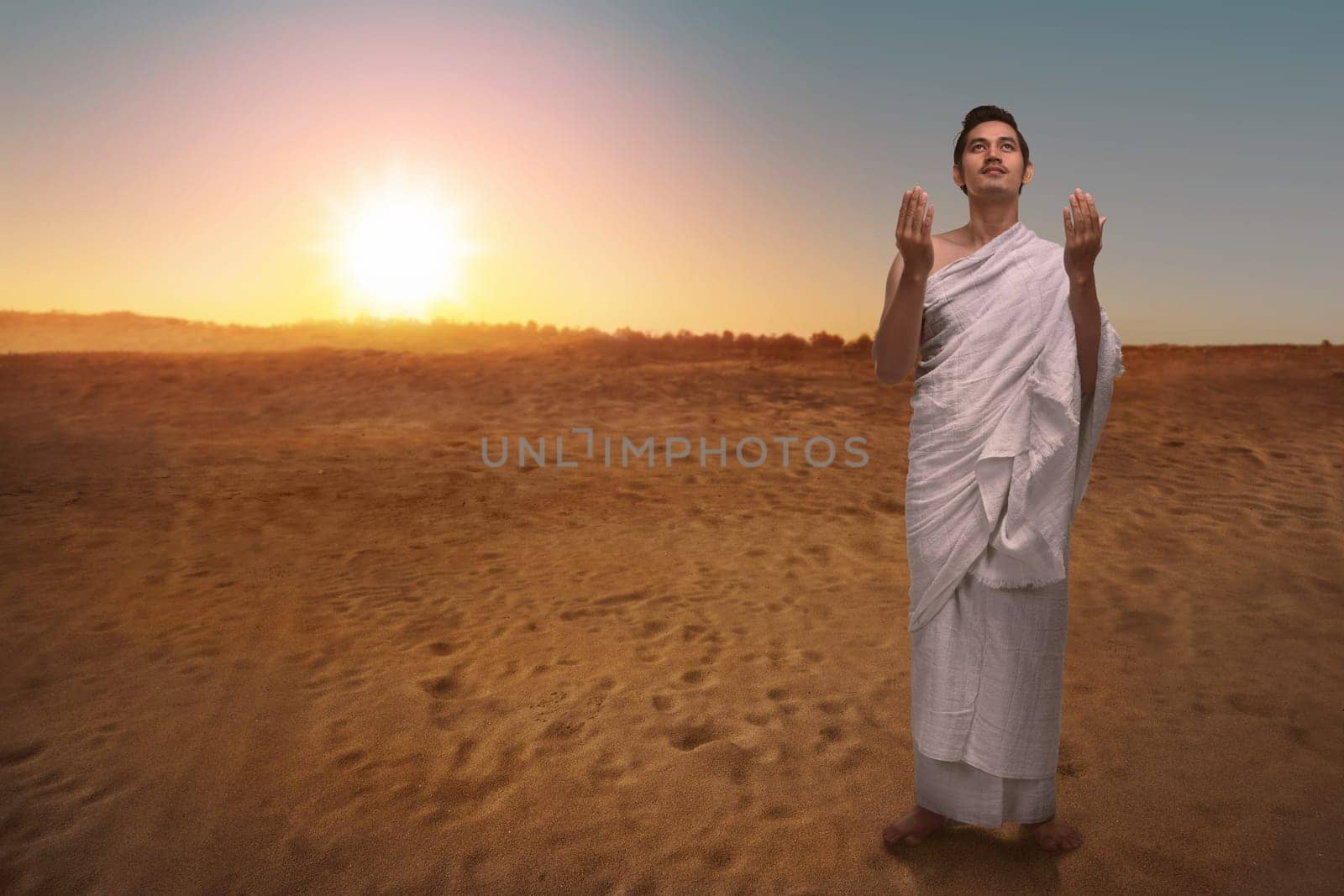 Religious asian muslim man in ihram praying to god with desert view background