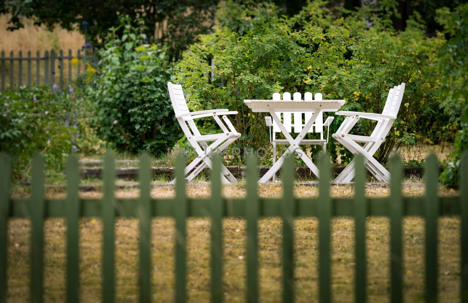 Garden chairs and table behind fence. Green grass and trees. Sweden, Europe, Scandinavia.