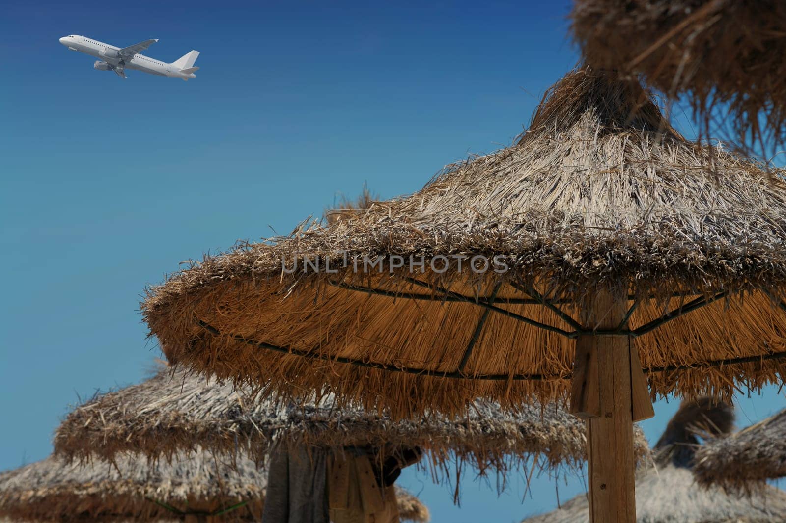 Parasol made of straw in the cloudless blue sky a passenger plane..