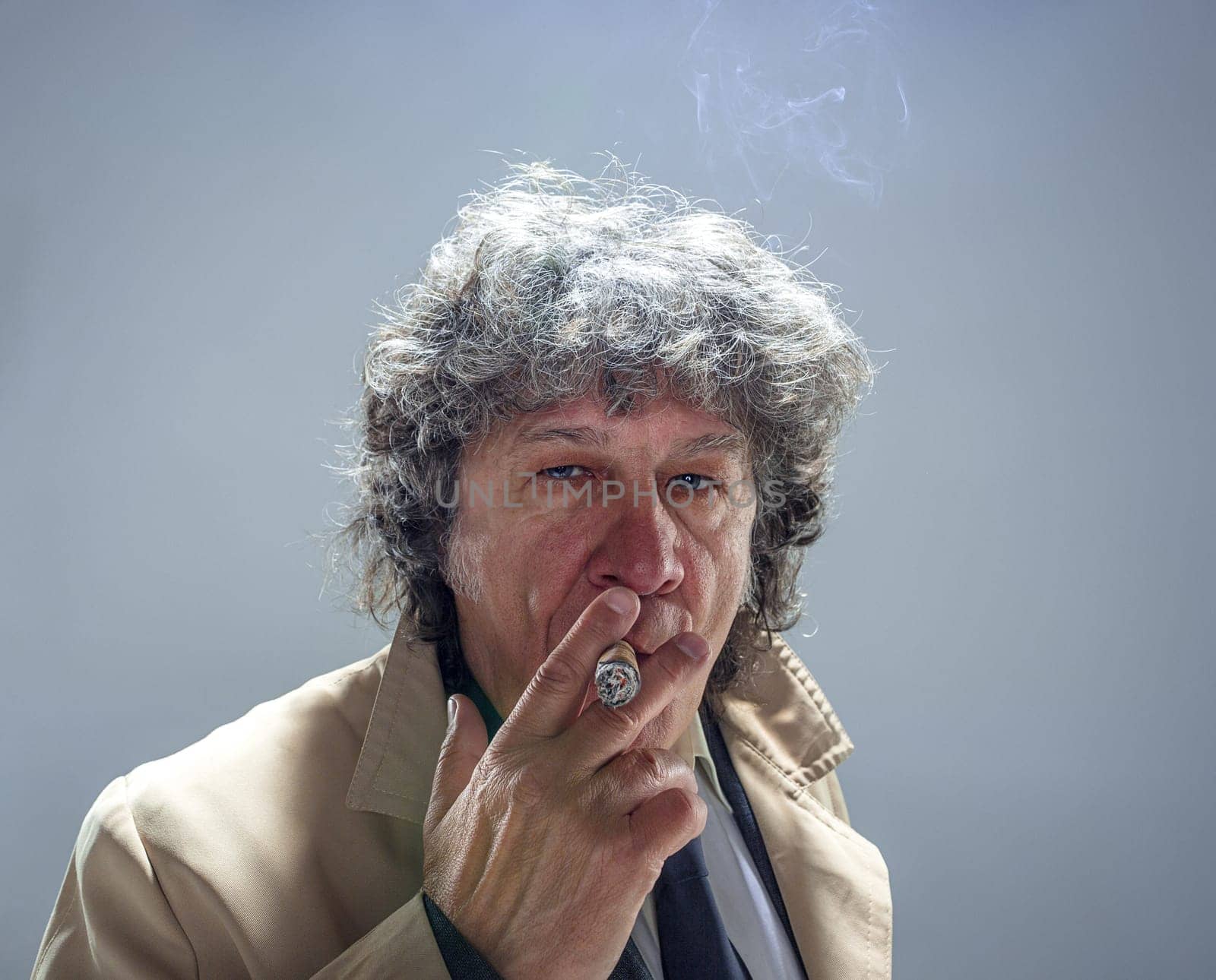The senior man in cloak with cigar as detective or mafia boss. Studio shot on gray in retro stile