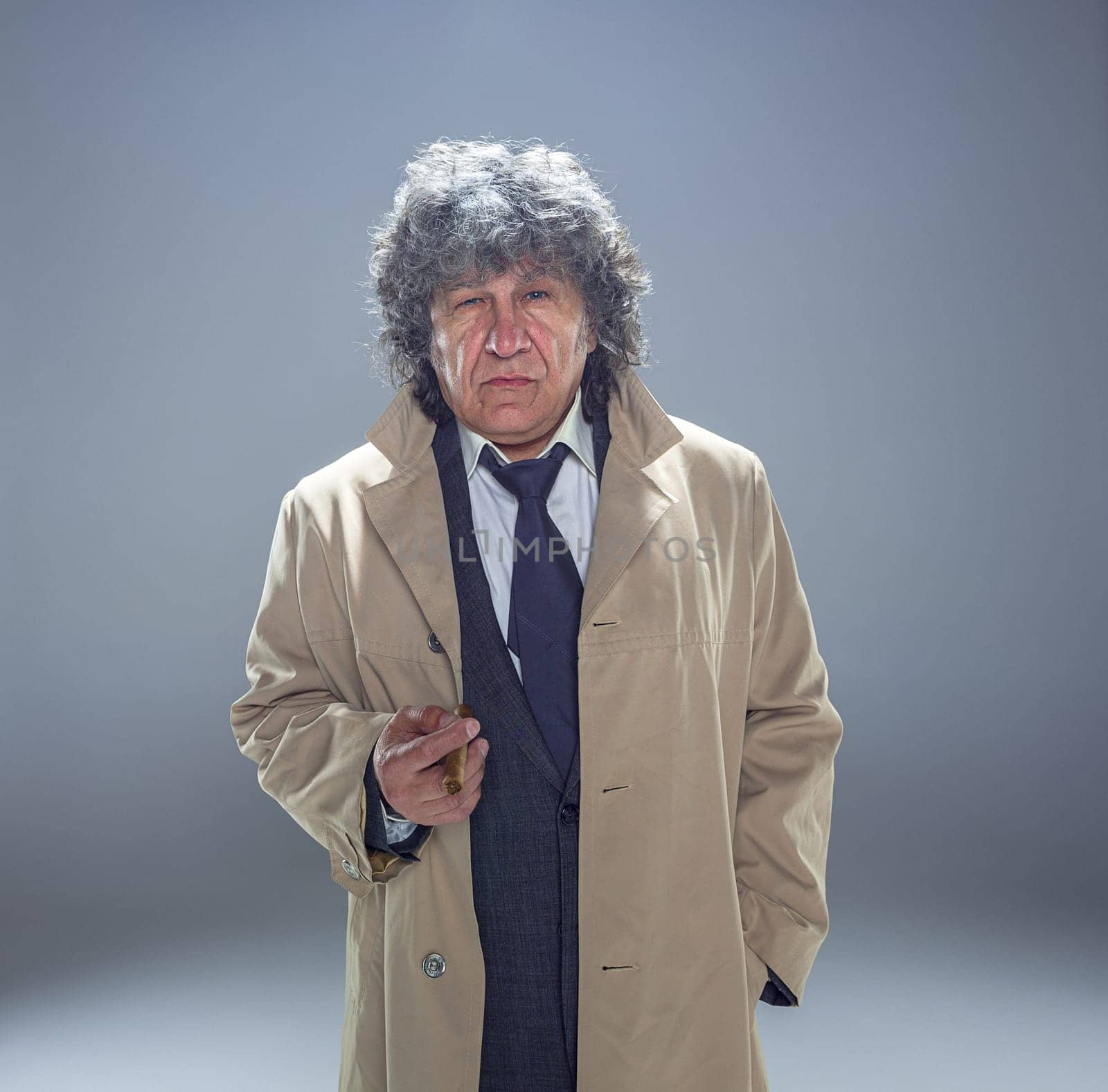 The senior man in cloak with cigar as detective or mafia boss. Studio shot on gray in retro stile
