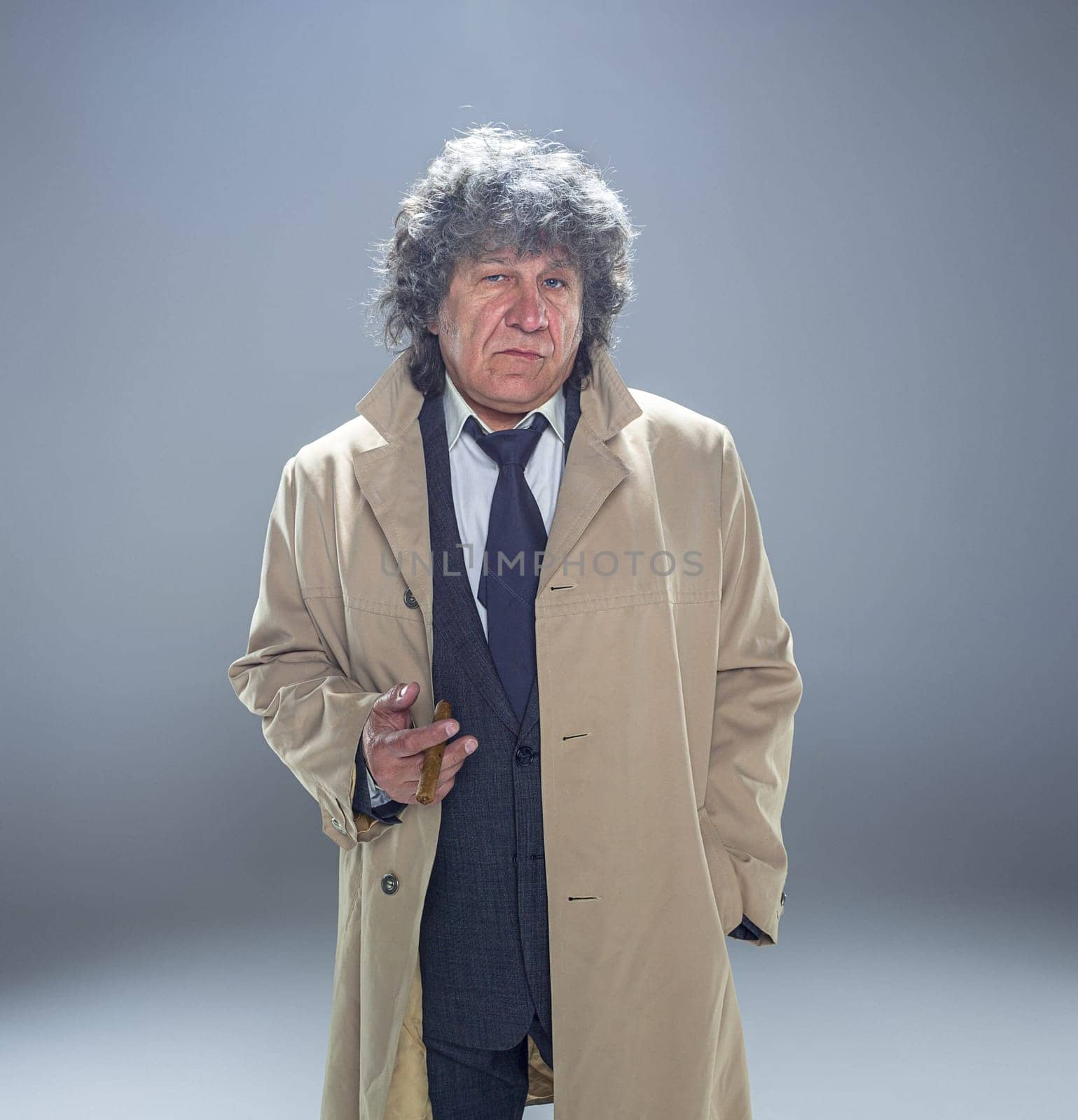 The senior man in cloak with cigar as detective or mafia boss. Studio shot on gray in retro stile