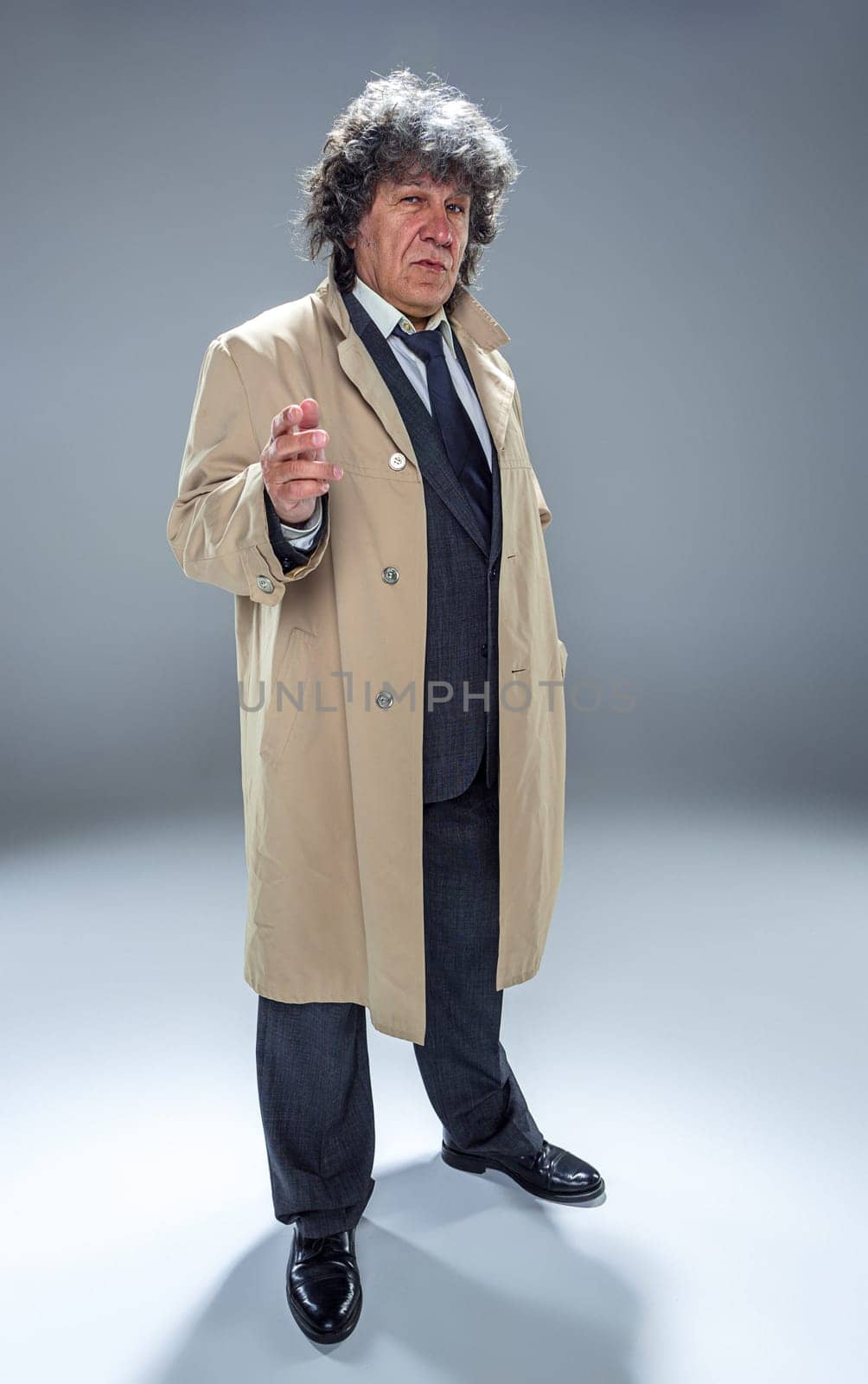 The senior man in cloak as detective or mafia boss. Studio shot on gray in retro stile