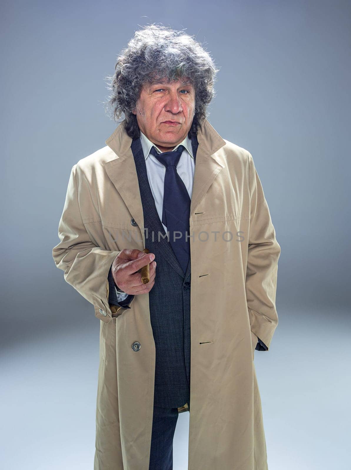 The senior man in cloak with cigar as detective or mafia boss. Studio shot on gray in retro stile