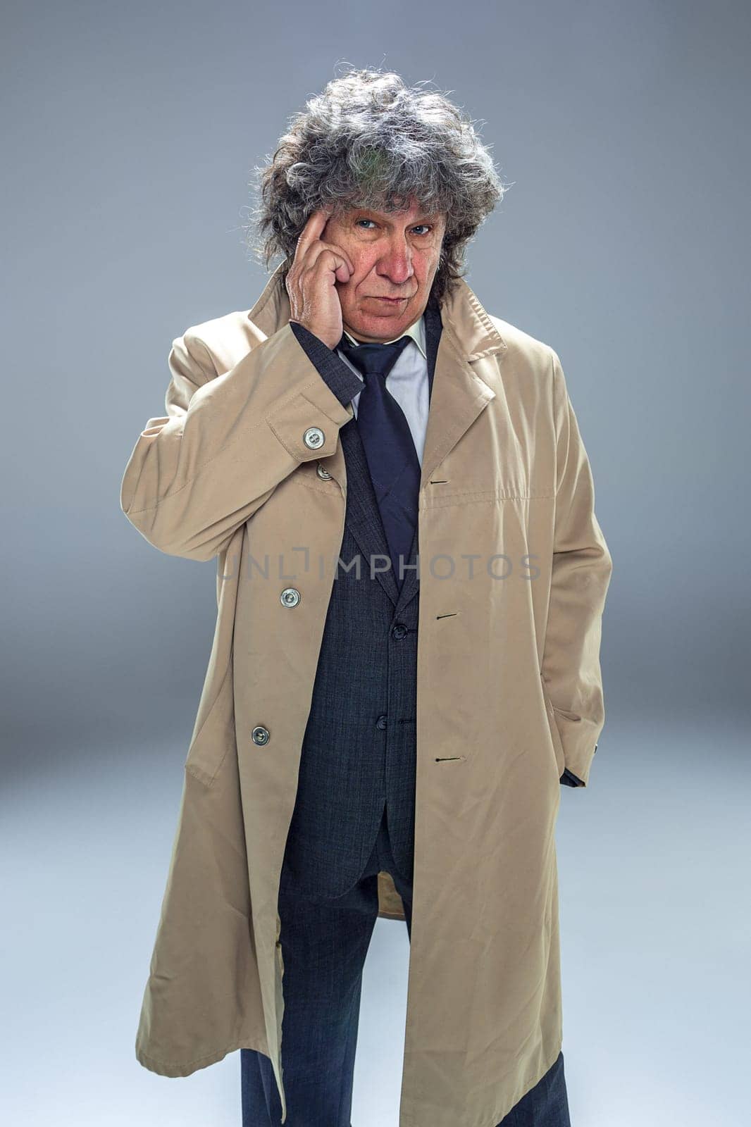 The senior man in cloak as detective or mafia boss. Studio shot on gray in retro stile